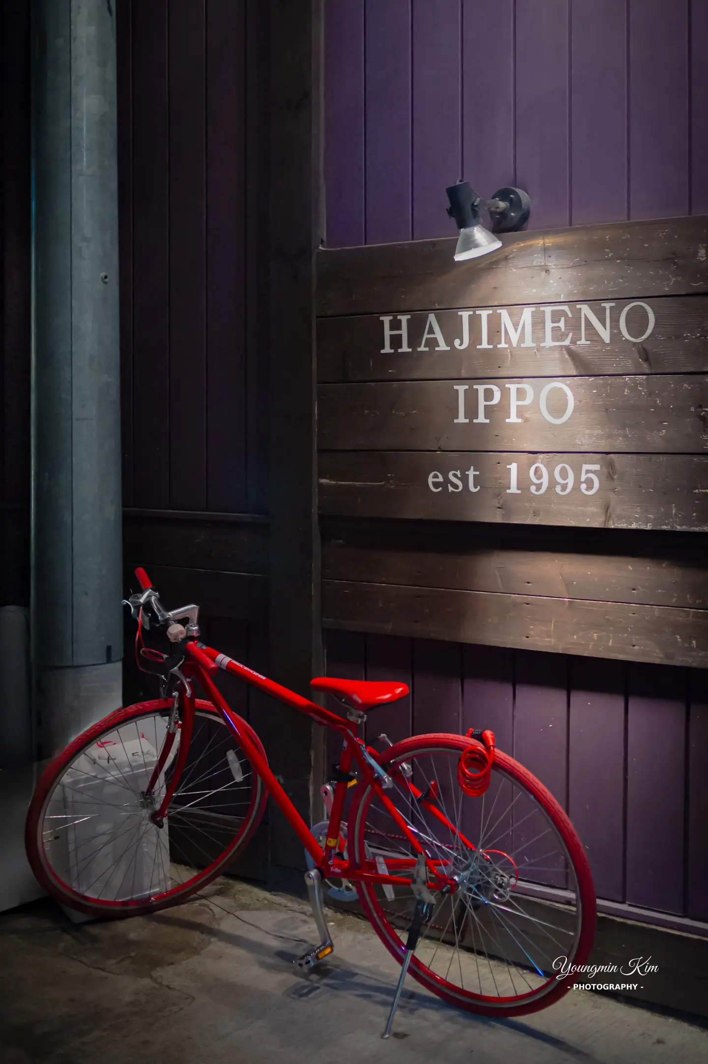 A red bicycle beneath the illuminated Hajime no Ippo sign at night in Japan