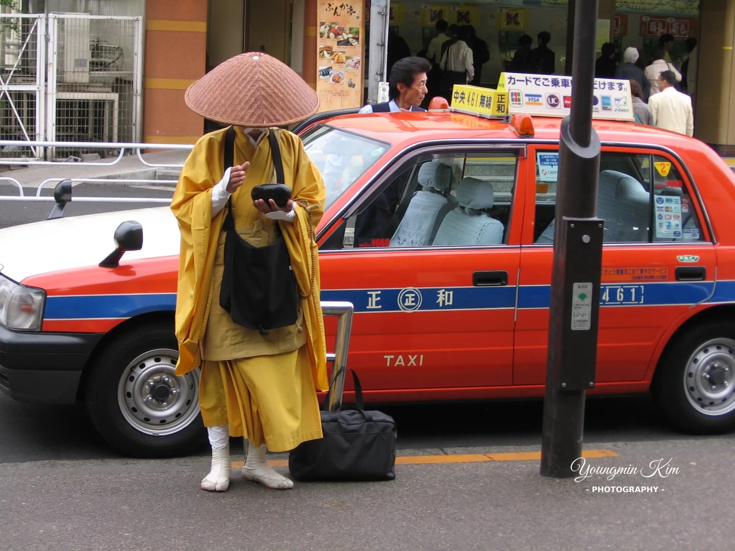 A monk walking along a Tokyo street beside a taxi