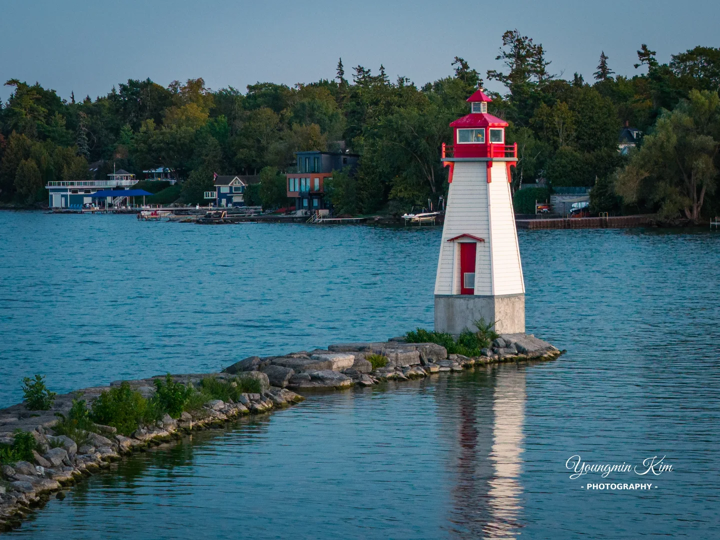 A red-and-white lighthouse at Jackson's Point, reached by a diagonal stone breakwater across blue water